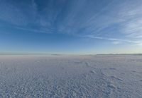 the vast expanse is covered in snow and clouds under a blue sky, with a lone person walking on one side