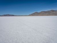 a white field with mountains and blue sky behind it and tracks of people running in the distance