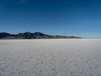 the lone person stands alone in an empty plain with mountains in the background, a cloudless blue sky