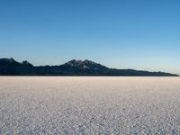 the lone person stands alone in an empty plain with mountains in the background, a cloudless blue sky