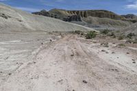 a dirt road surrounded by rocky formations under a blue sky, near a dry plain