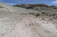 a dirt road surrounded by rocky formations under a blue sky, near a dry plain