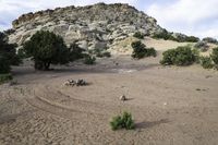 a sandy area with dirt in front of rocks and trees on the side of a mountain