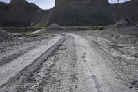 an empty dirt road passing through a mountain with a telephone pole and telephone wires over it