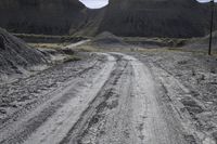 an empty dirt road passing through a mountain with a telephone pole and telephone wires over it