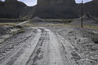 an empty dirt road passing through a mountain with a telephone pole and telephone wires over it