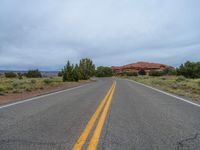 a empty long road with a yellow line painted down the middle of the street and in between two bushes, a red rock formation is visible in the background