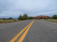 a empty long road with a yellow line painted down the middle of the street and in between two bushes, a red rock formation is visible in the background