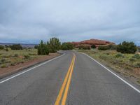 a empty long road with a yellow line painted down the middle of the street and in between two bushes, a red rock formation is visible in the background