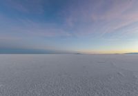 an aerial photograph of a lone snow capped beach with clouds in the sky as the sun goes down