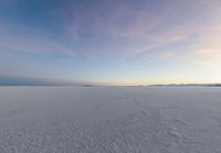 an aerial photograph of a lone snow capped beach with clouds in the sky as the sun goes down