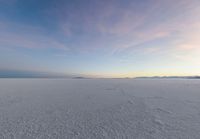 an aerial photograph of a lone snow capped beach with clouds in the sky as the sun goes down