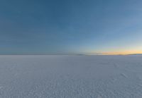 an icy field with snow and mountains in the distance at dusk with clear skies above