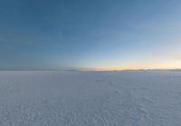 an icy field with snow and mountains in the distance at dusk with clear skies above