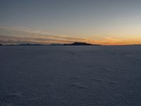 snow covered landscape with mountains in the distance at sunset time, showing footprints in the ice