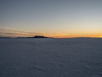 snow covered landscape with mountains in the distance at sunset time, showing footprints in the ice