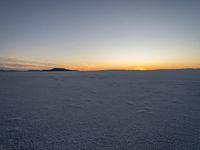 snow covered landscape with mountains in the distance at sunset time, showing footprints in the ice