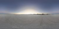 a snowmobile parked in the middle of a flat, empty snow field with a sky and mountains in the background