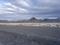 an empty road with no traffic in the distance surrounded by mountains and dry grass and bushes