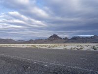 an empty road with no traffic in the distance surrounded by mountains and dry grass and bushes