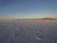 a person standing alone on an open plain in the snow, with a mountain in the background