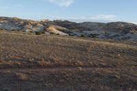 a man is walking along the dirt trail in the desert towards a rock formation in the distance