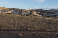 a man is walking along the dirt trail in the desert towards a rock formation in the distance