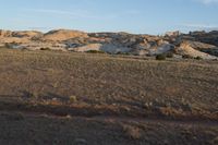 a man is walking along the dirt trail in the desert towards a rock formation in the distance