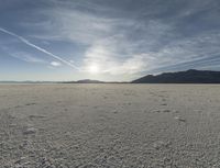 an empty sandy plain in the desert under a blue sky with sparse clouds and mountain range behind