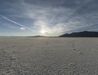 an empty sandy plain in the desert under a blue sky with sparse clouds and mountain range behind