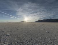 an empty sandy plain in the desert under a blue sky with sparse clouds and mountain range behind