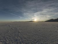 the sunset lights up the distance across the snow - covered desert landscape in the middle