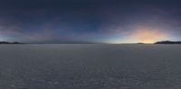 a panoramic view of a snow covered plain at sunset with sun rising over mountains