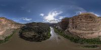 a wide river running past large mountains under a cloudy sky in this fish - eye photograph