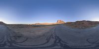 the panoramic image shows some sort of desert with rocks in the distance and on each end a long path is surrounded by grass