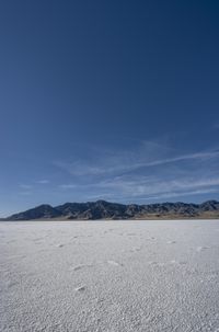 an empty vast plain covered in white sand with mountains in the distance and a blue sky