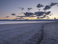 an empty beach with a few clouds and mountains in the background at sunset time with one plant growing from a crack in the sand