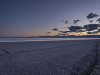 an empty beach with a few clouds and mountains in the background at sunset time with one plant growing from a crack in the sand