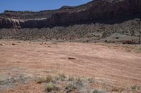 a dirt road through a desert plain with a mountain behind it and a clear blue sky in the background