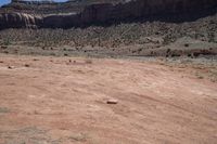 a dirt road through a desert plain with a mountain behind it and a clear blue sky in the background