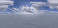 a snow covered field with clouds over it and a man on a snowboard next to it