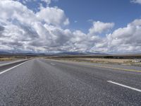 a highway and the road is lined with clouds and mountains in background of picture on a bright sunny day