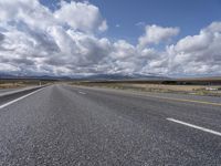 a highway and the road is lined with clouds and mountains in background of picture on a bright sunny day