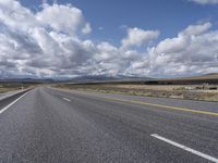 a highway and the road is lined with clouds and mountains in background of picture on a bright sunny day