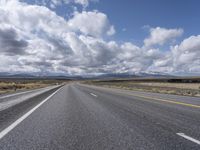 a highway and the road is lined with clouds and mountains in background of picture on a bright sunny day