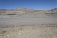 a dirt road is surrounded by some hills and desert like terrain as the vehicle sits on it