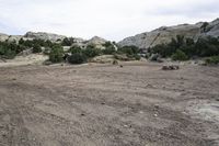 a dirt field with trees and rocks on it on a partly cloudy day in an area