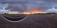 a road under a cloudy sky with a person on it at sunset in the distance