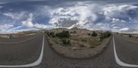 a highway and the mountains under a cloudy sky in a panorama lens of a wide road