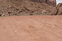 a person riding on an orange motorcycle across a dirt field with mountains in the background